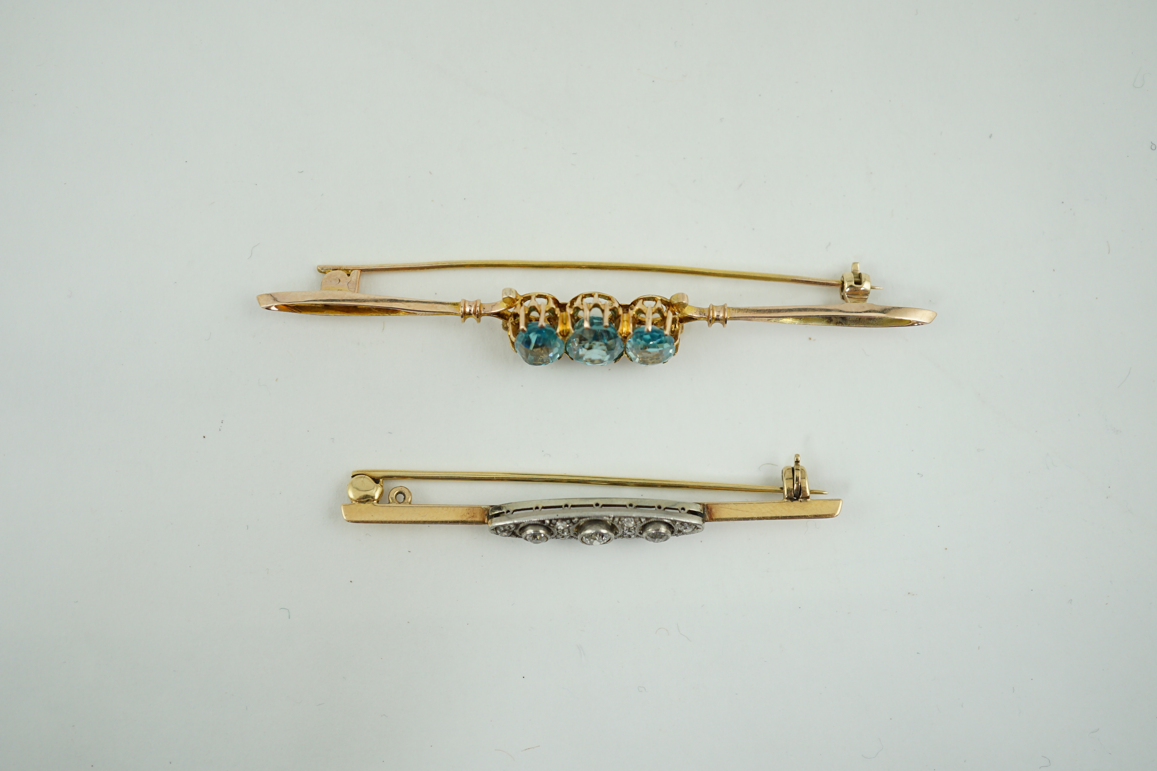 A 1920's yellow metal and millegrain diamond cluster set bar brooch, 56mm, together with a yellow metal and three stone blue zircon set bar brooch